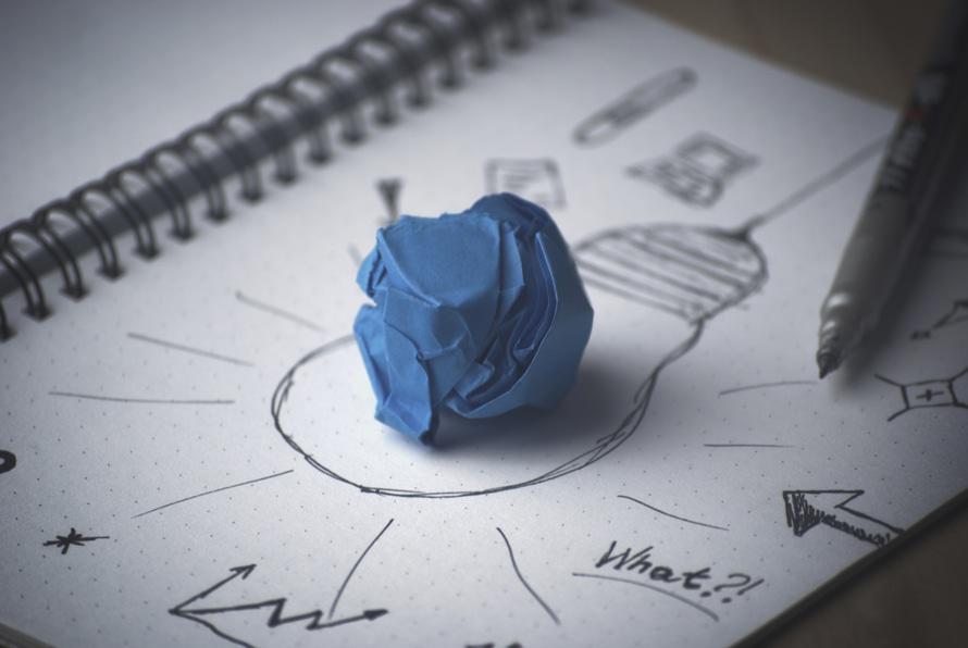 Das Bild zeigt einen Schreibblock mit einer gezeichneten Glühbirne und einem zerknüllten Papier. Es steht als Symbol für die Ideenfindung und die Denkarbeit zu Beginn der Arbeit an Ihrer eigenen Website.